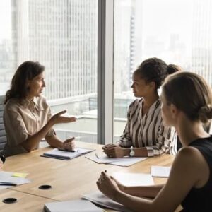 Tre kvinnor diskuterar vid ett mötesbord med dokument och anteckningar